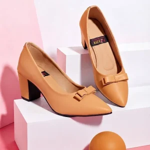 Women's beige pointed toe block heel pumps with decorative bow detail displayed on white podiums against a pink studio background.