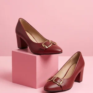 Women's maroon block heel pumps with elegant gold buckle detail, round toe, and comfortable dress shoe design displayed on pink studio blocks.