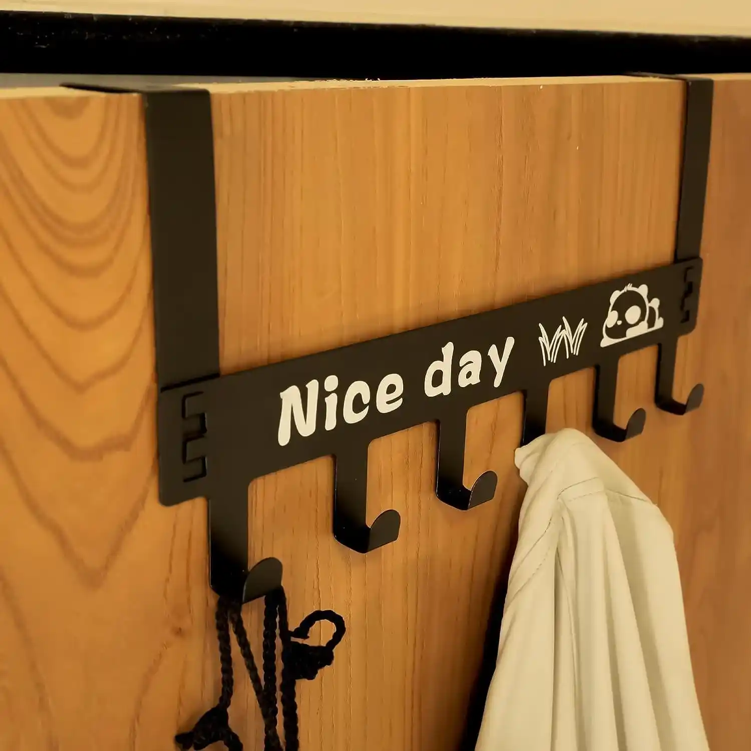 Black metal over-the-door hook hanger featuring six hooks and a panda Nice Day graphic being placed on a door 1
