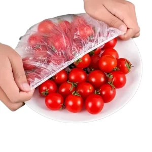 Four-step instructional grid showing hands stretching a clear elastic plastic food cover over a bowl of fresh red and green tomatoes.