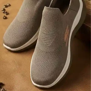 Pair of light brown knit slip-on walking shoes resting on a rustic wooden beam. 1