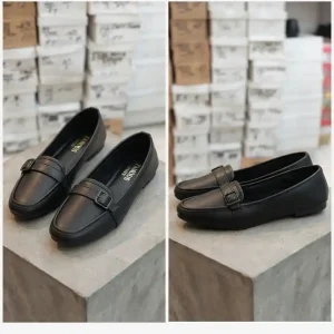 Pair of women's blackslip-on loafers with decorative matching buckles displayed on a stone pedestal.
