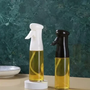 Two clear glass cooking oil sprayer bottles filled with golden oil, featuring white and black ergonomic trigger pump heads on a countertop.