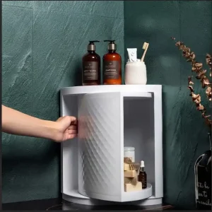 White single-layer 360-degree rotating corner bathroom cabinet with dual storage tiers, cosmetics, and a top jewelry tree holder against green tiles.