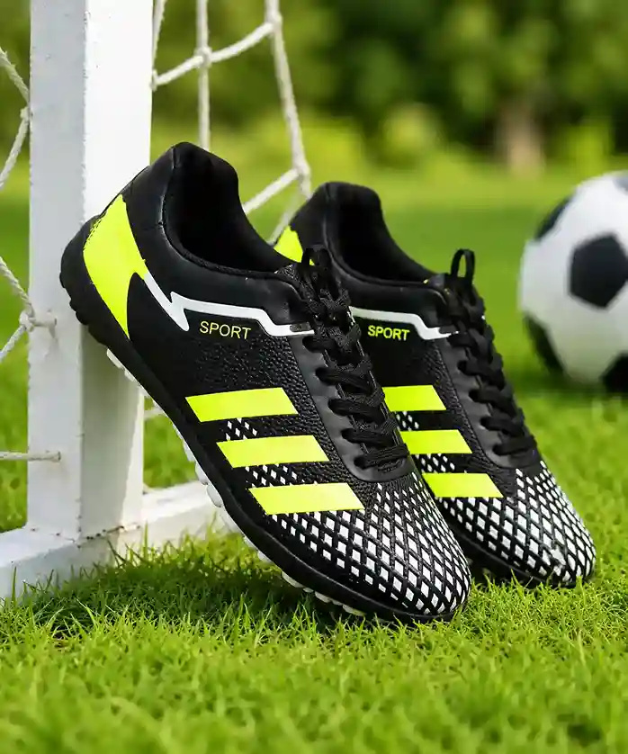 black football cleat with neon yellow stripes leaning against a soccer goal post on a green turf field.